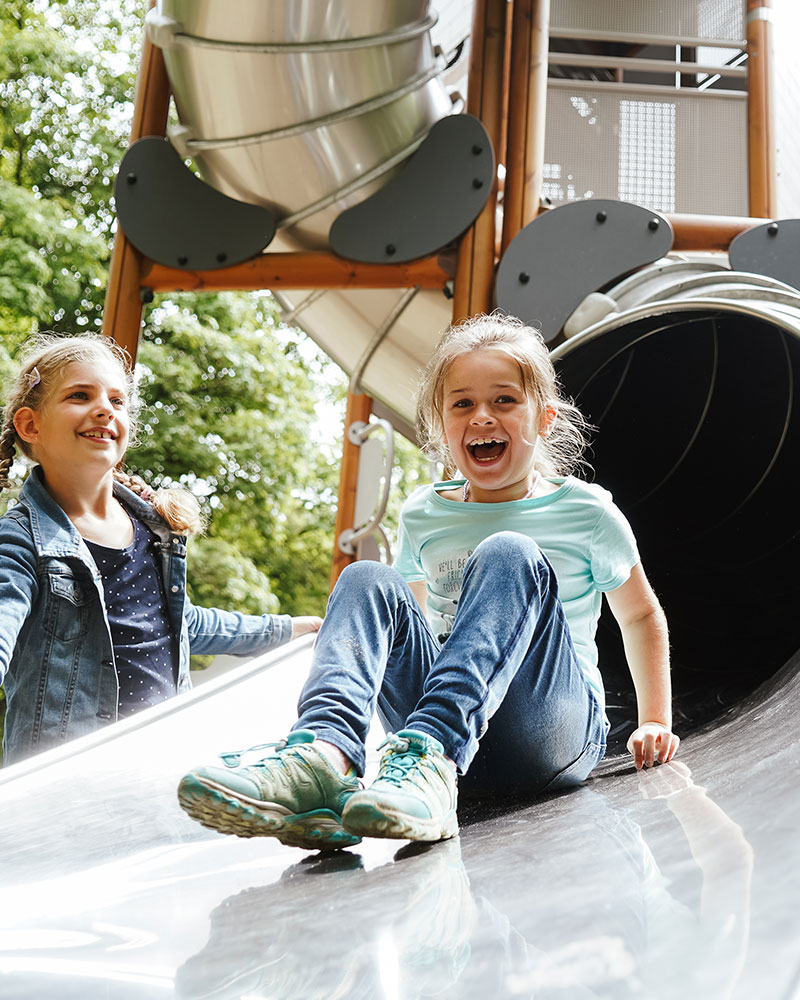 Une jeune fille glisse sur un grand toboggan tubulaire, la bouche ouverte d'excitation et de rire.